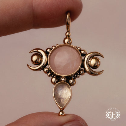 Selene brass pendant with pink stone held between fingers against a beige background