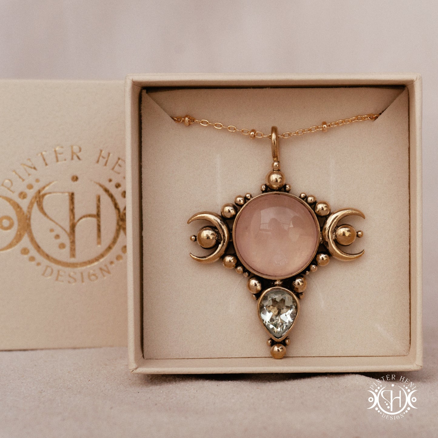 Selene brass pendant with pink stone held between fingers against a beige background