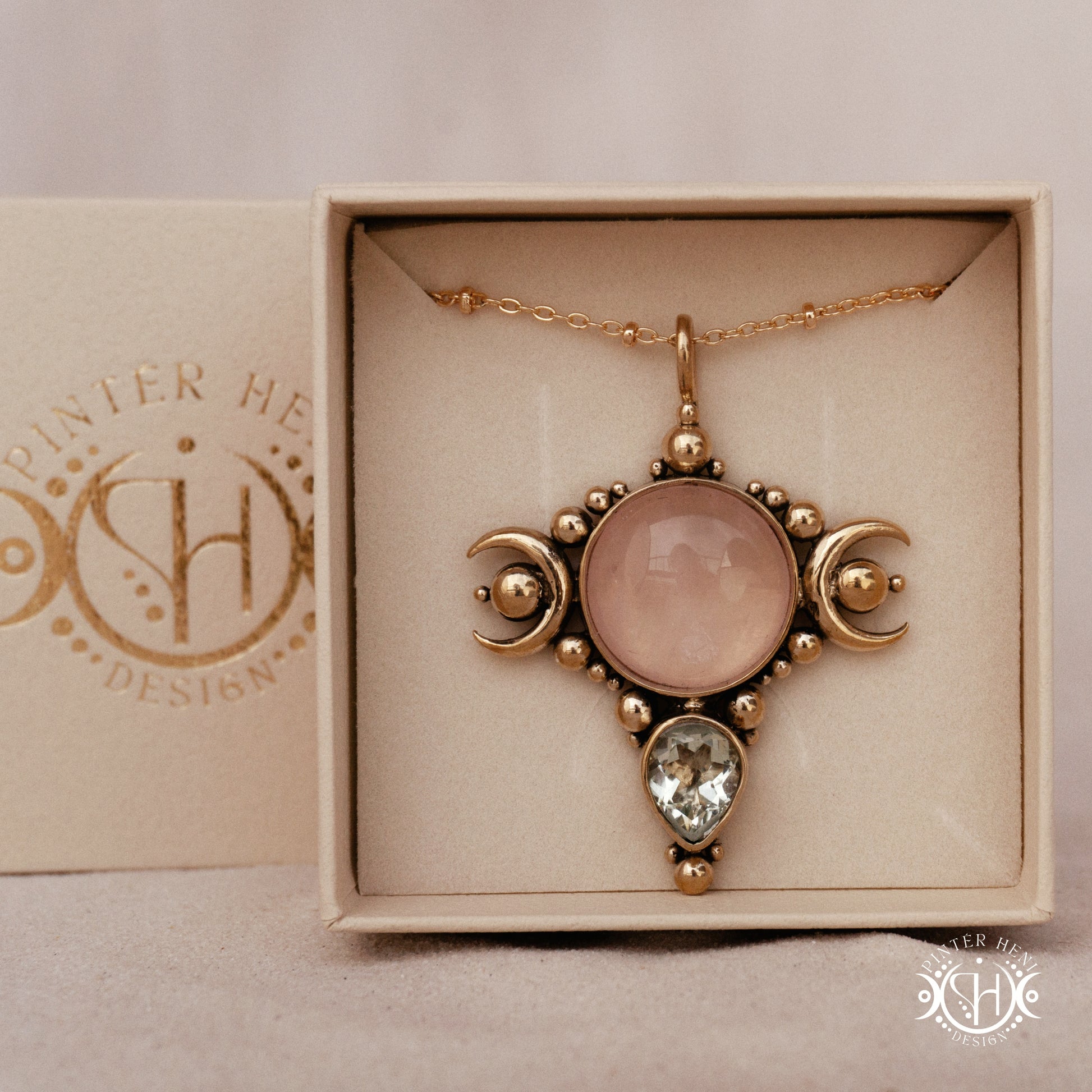 Selene brass pendant with pink stone held between fingers against a beige background