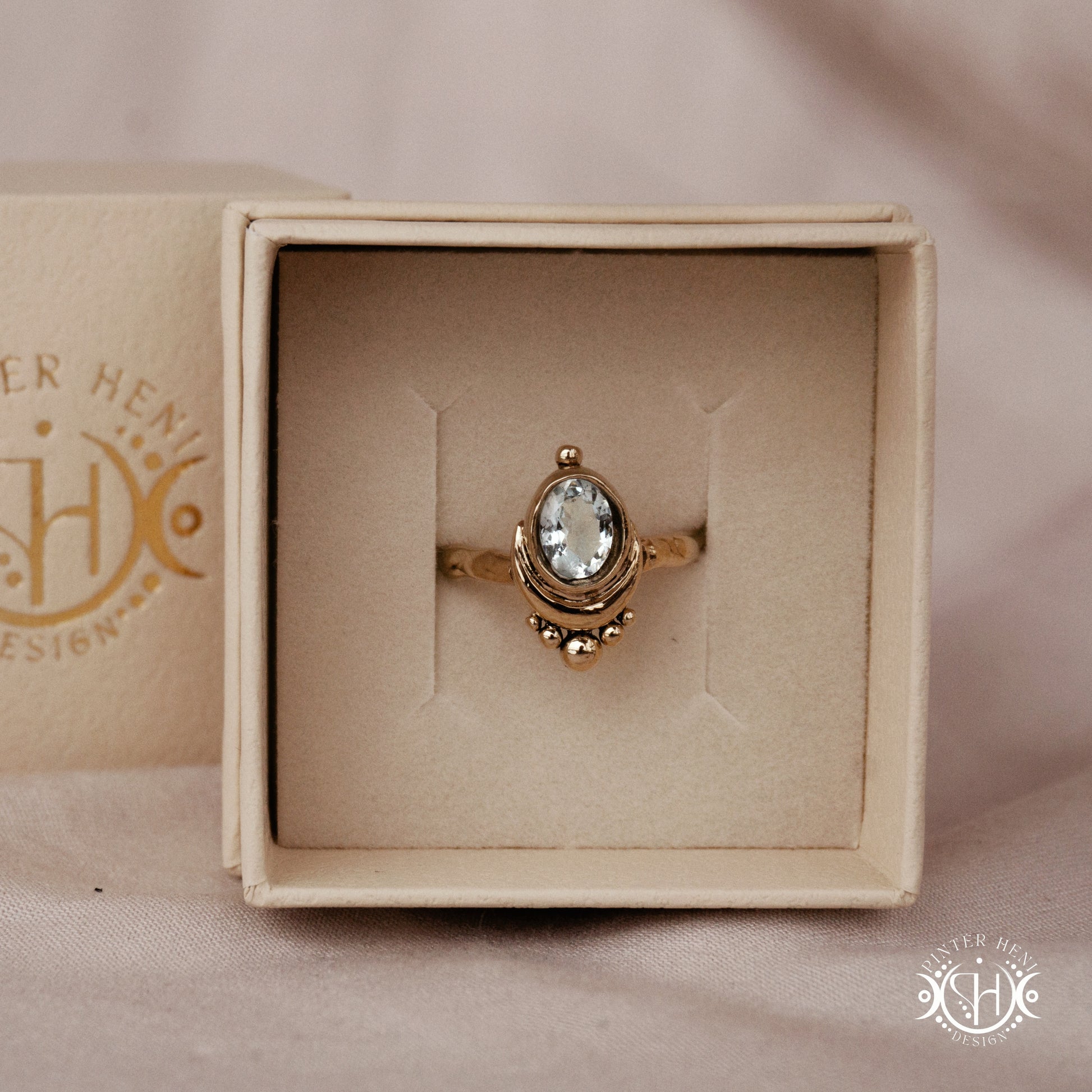 Handmade oval aquamarine gemstone ring set within a crescent-inspired form, in branded jewelry box.