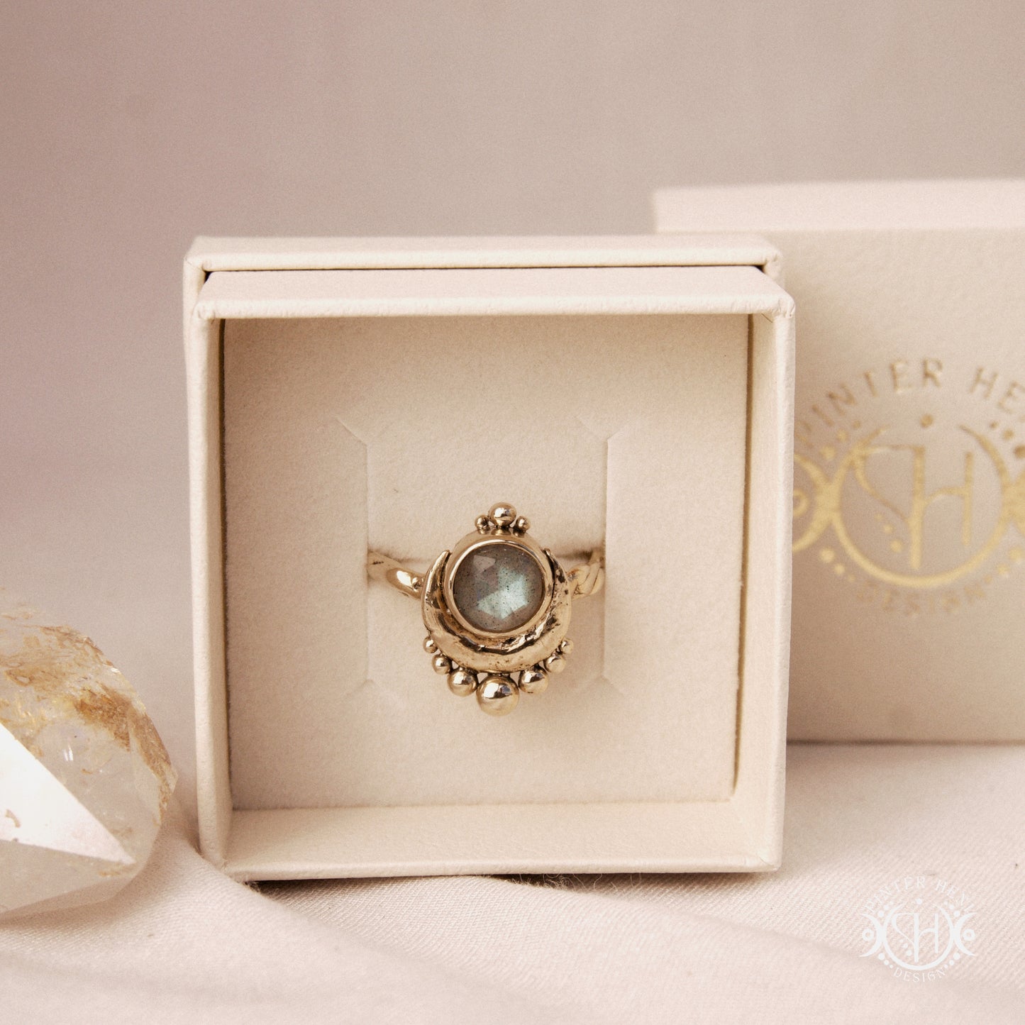 Handmade crescent moon ring with round labradorite set inside the lunar curve, in a branded jewelry box.