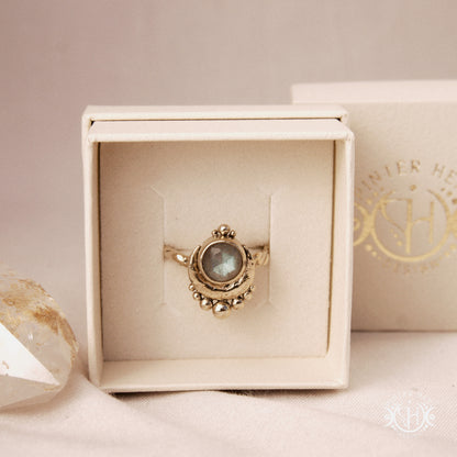 Handmade crescent moon ring with round labradorite set inside the lunar curve, in a branded jewelry box.