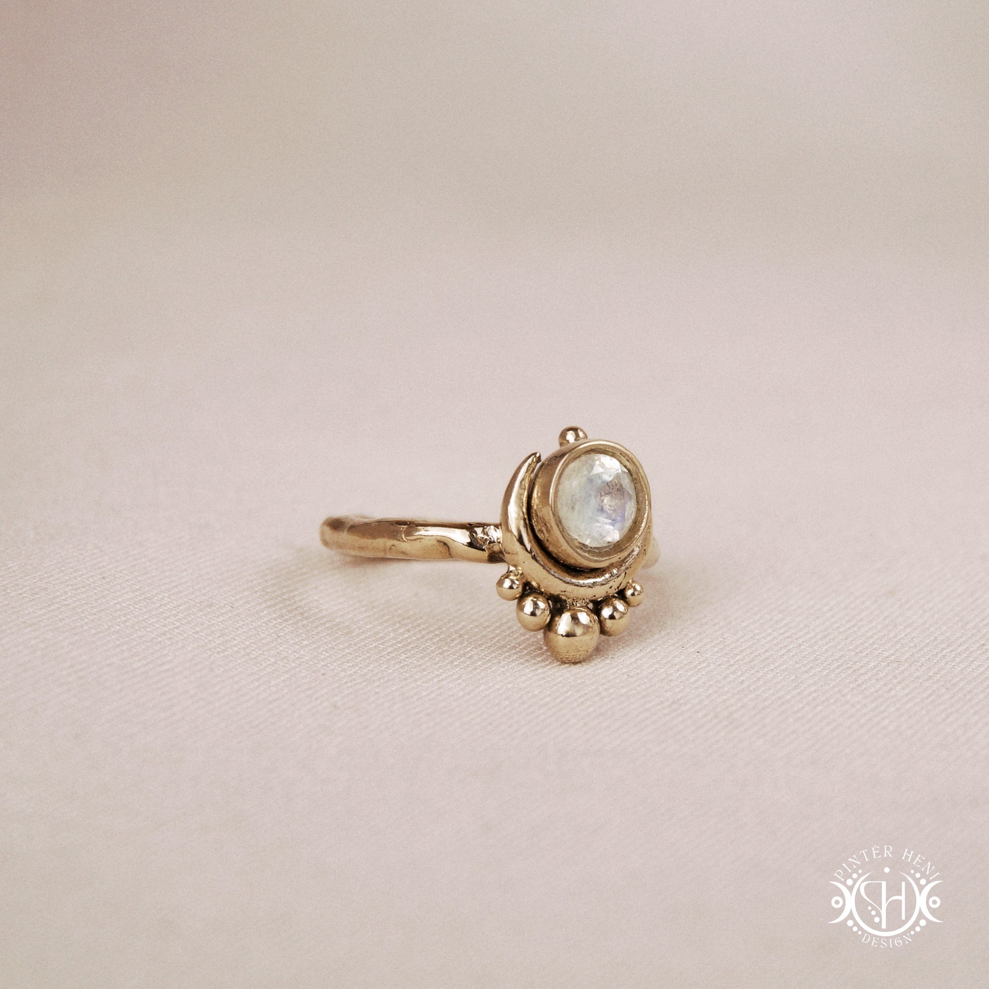 Handmade crescent moon ring with round moonstone set inside the lunar curve, on beige textile.