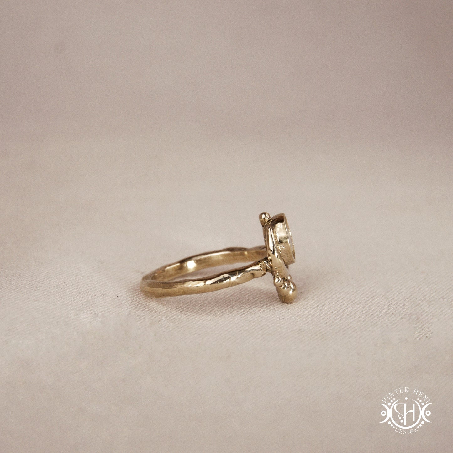 Handmade crescent moon ring with round moonstone set inside the lunar curve, on beige textile.