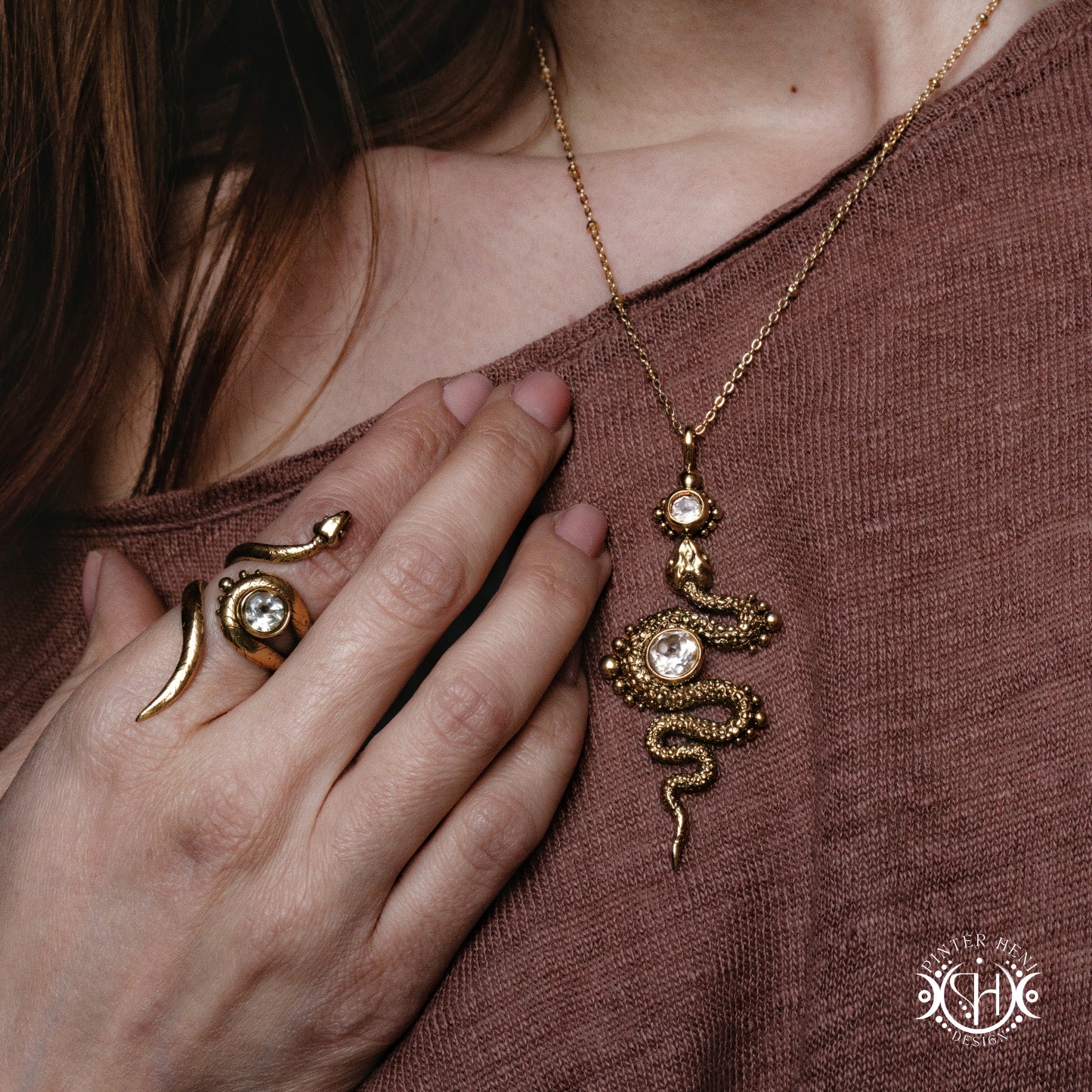 Gold snake necklace and ring on a person wearing a brown top.