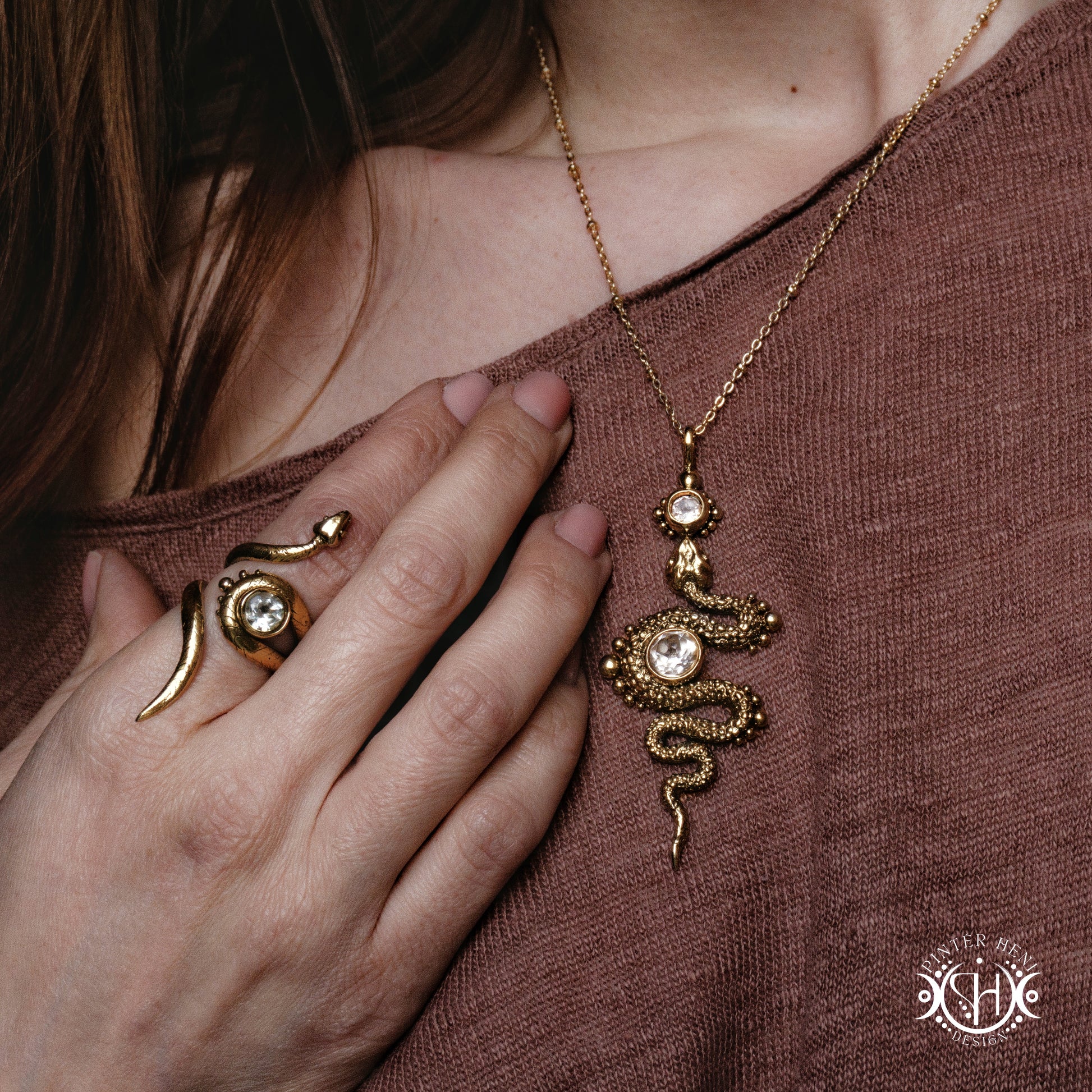Gold snake necklace and ring on a person wearing a brown top.