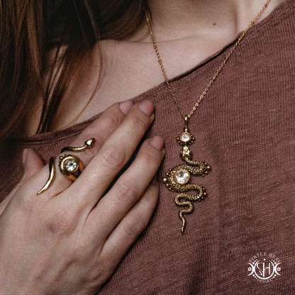 Gold snake necklace and ring on a person wearing a brown top.