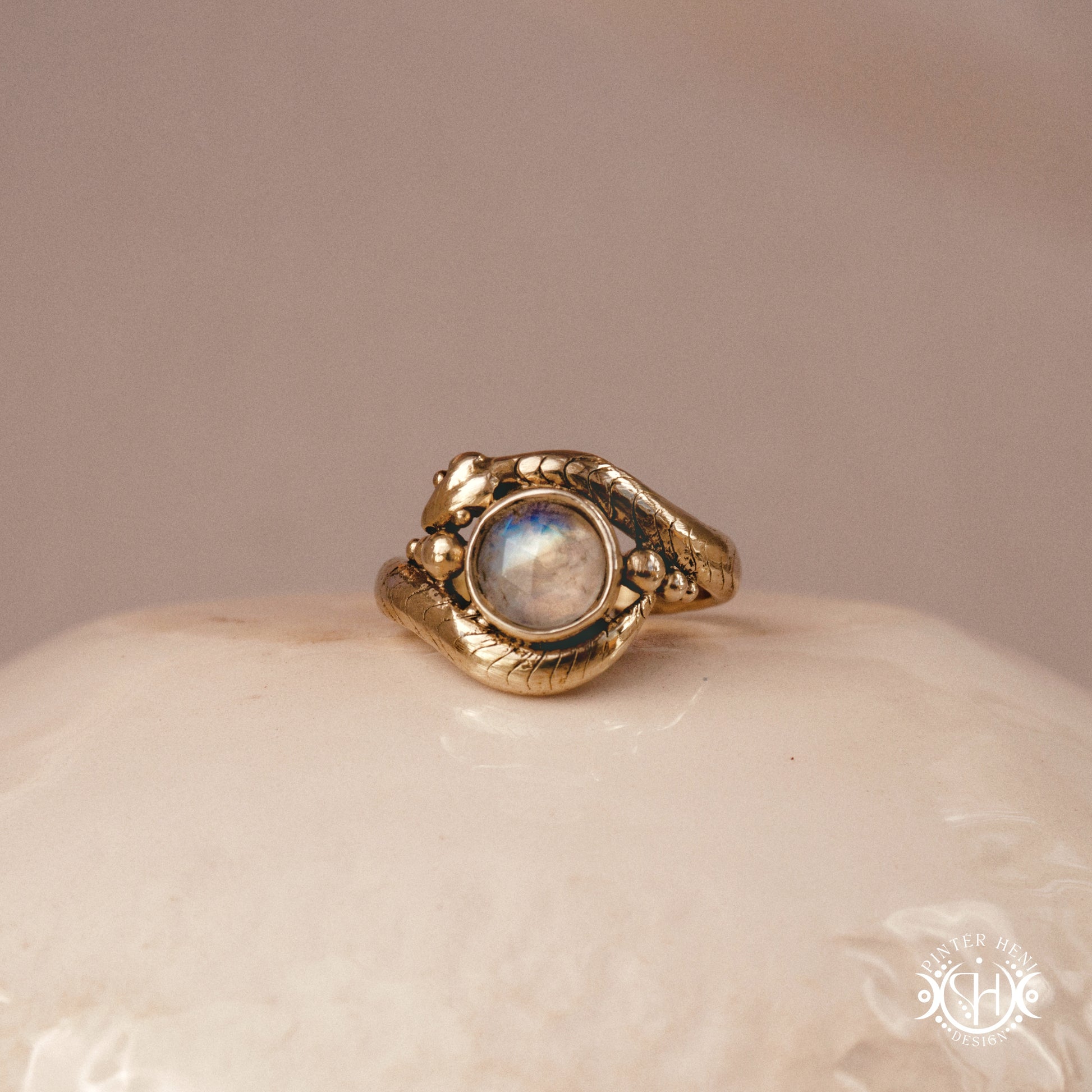 Handmade serpent ring set with moonstone, sculptural wax carved design in brass, silver, or solid gold, on ceramic surface.