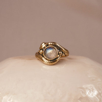 Handmade serpent ring set with moonstone, sculptural wax carved design in brass, silver, or solid gold, on ceramic surface.