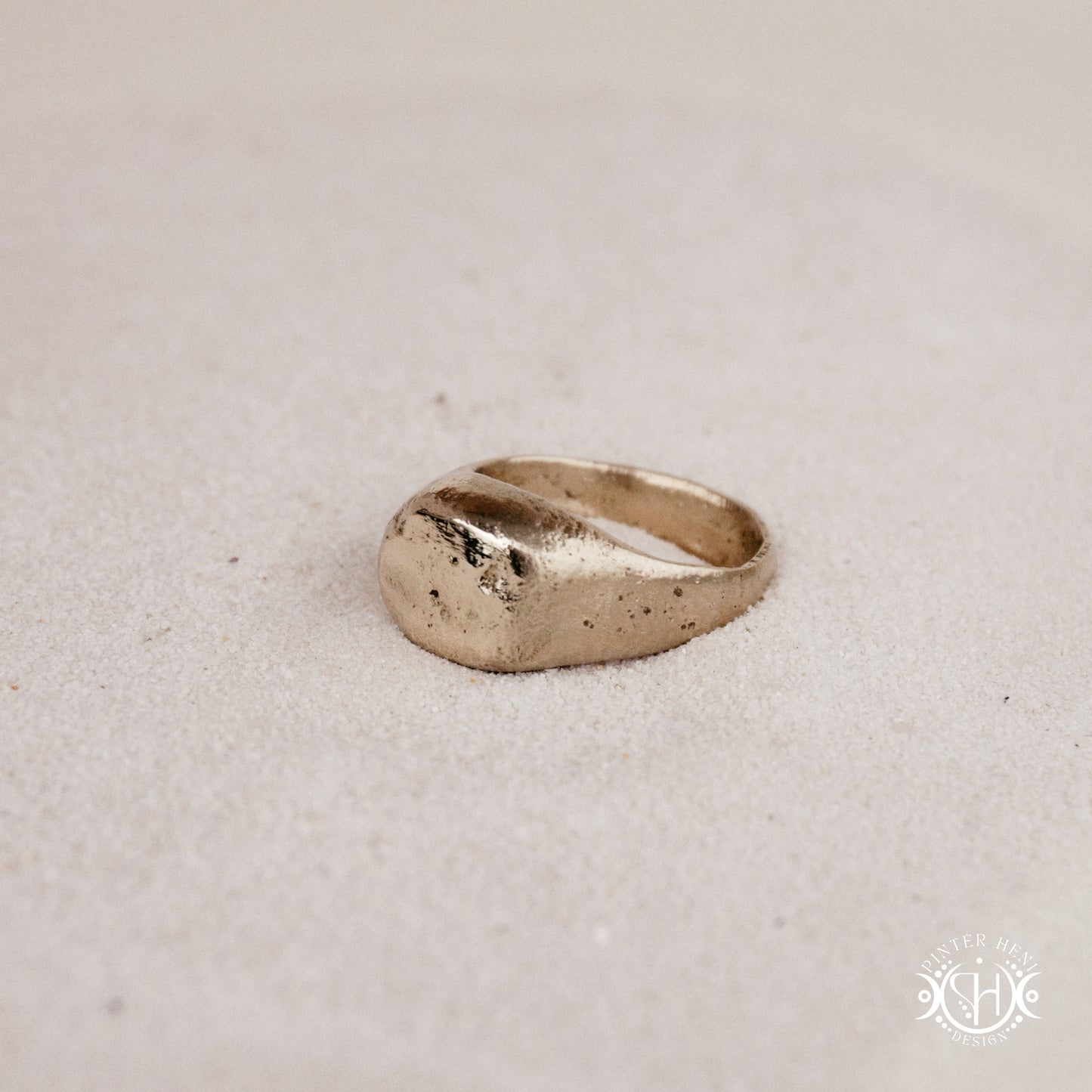 Sigil Ring handmade sandcast brass signet-style ring with raw surface and ancient-inspired sculptural form, in sand.