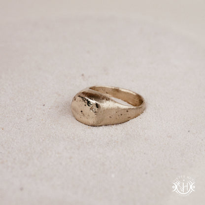 Sigil Ring handmade sandcast brass signet-style ring with raw surface and ancient-inspired sculptural form, in sand.