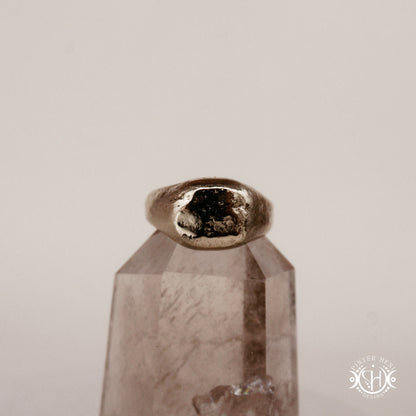 Sigil Ring handmade sandcast brass signet-style ring with raw surface and ancient-inspired sculptural form, in sand.