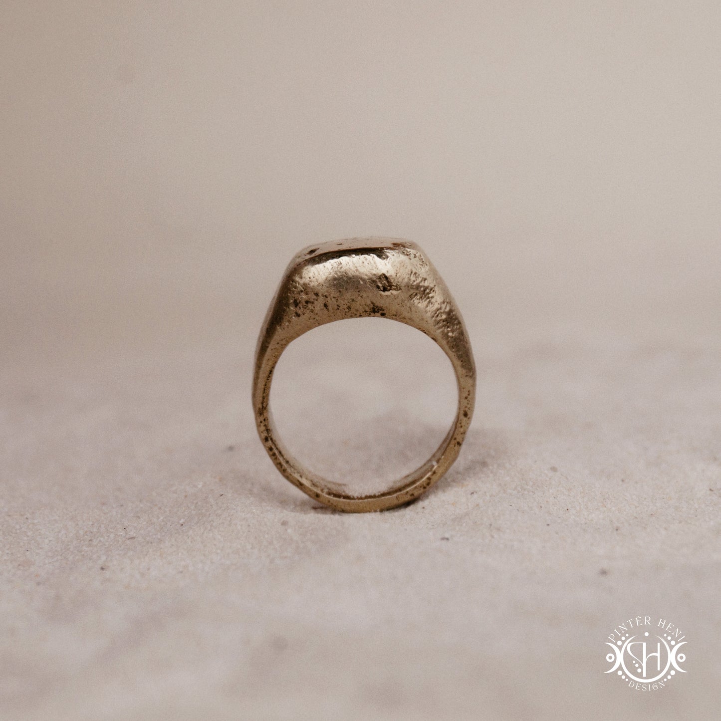 Sigil Ring handmade sandcast brass signet-style ring with raw surface and ancient-inspired sculptural form, in sand.