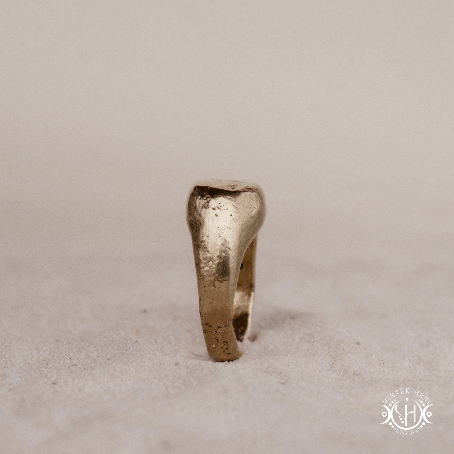 Sigil Ring handmade sandcast brass signet-style ring with raw surface and ancient-inspired sculptural form, in sand.