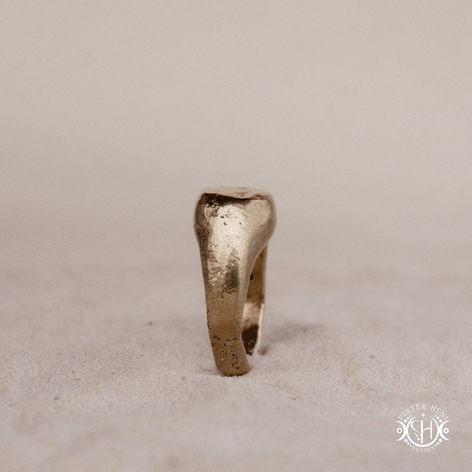 Sigil Ring handmade sandcast brass signet-style ring with raw surface and ancient-inspired sculptural form, in sand.