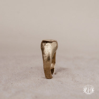 Sigil Ring handmade sandcast brass signet-style ring with raw surface and ancient-inspired sculptural form, in sand.