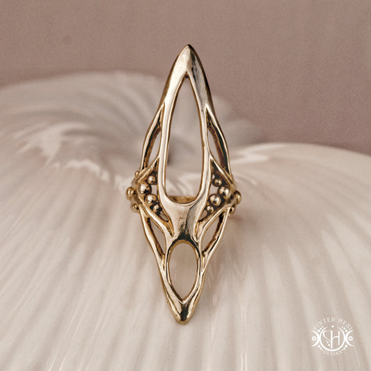 Zenith Ring sculptural vertical axial statement ring in brass, organic elongated handmade design, on ceramic surface.